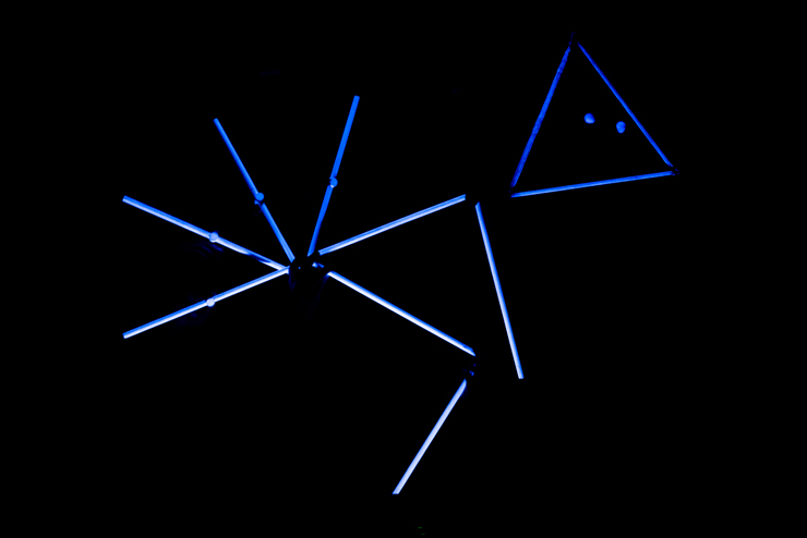 Na czarnym tle znajduje się konstelacja złożona z niebieskich, oświetlonych patyków, tworzących figury geometryczne. 